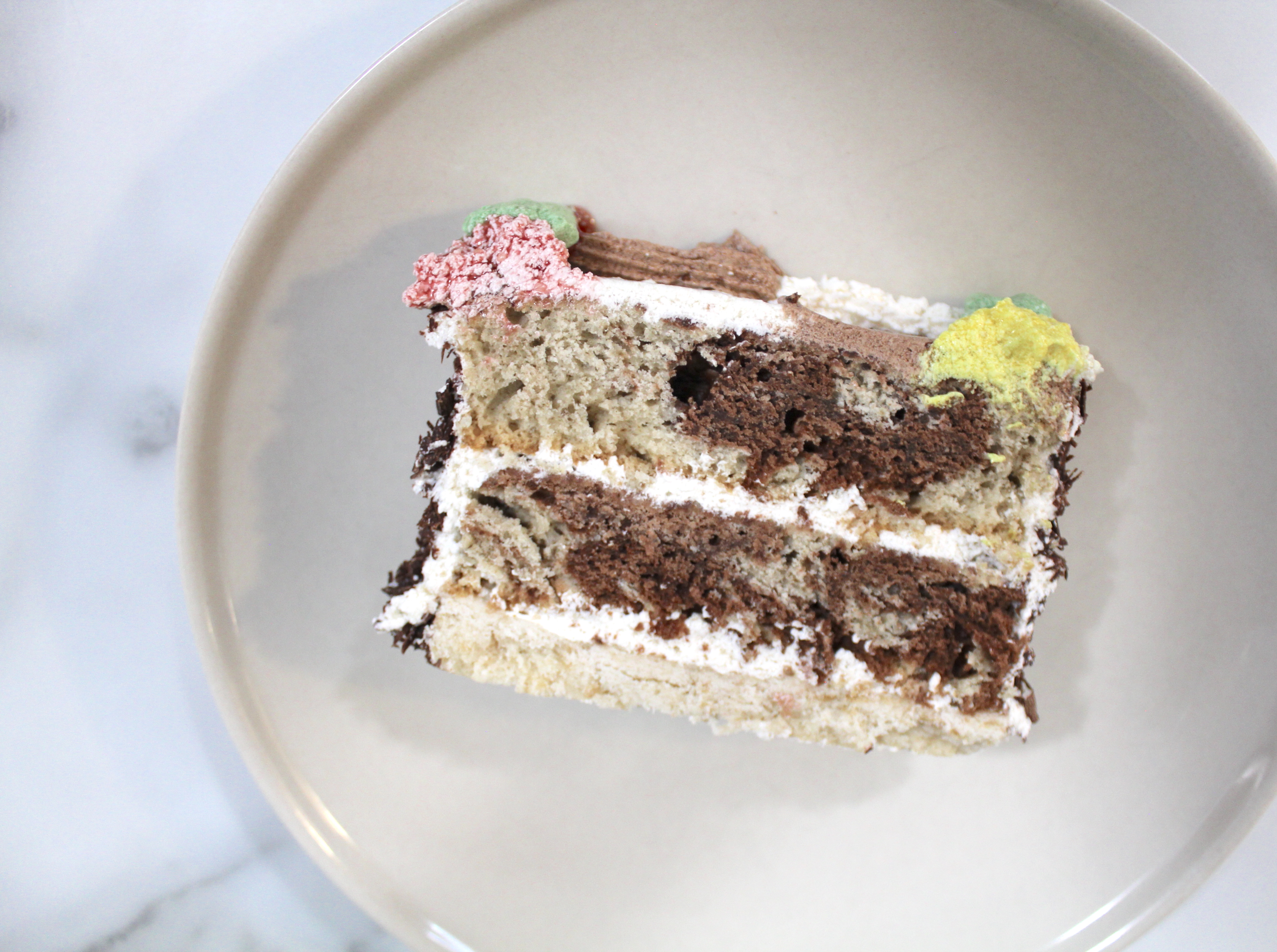 Slice of log cake. Cake has two marble layers with alternating vanilla frosting.