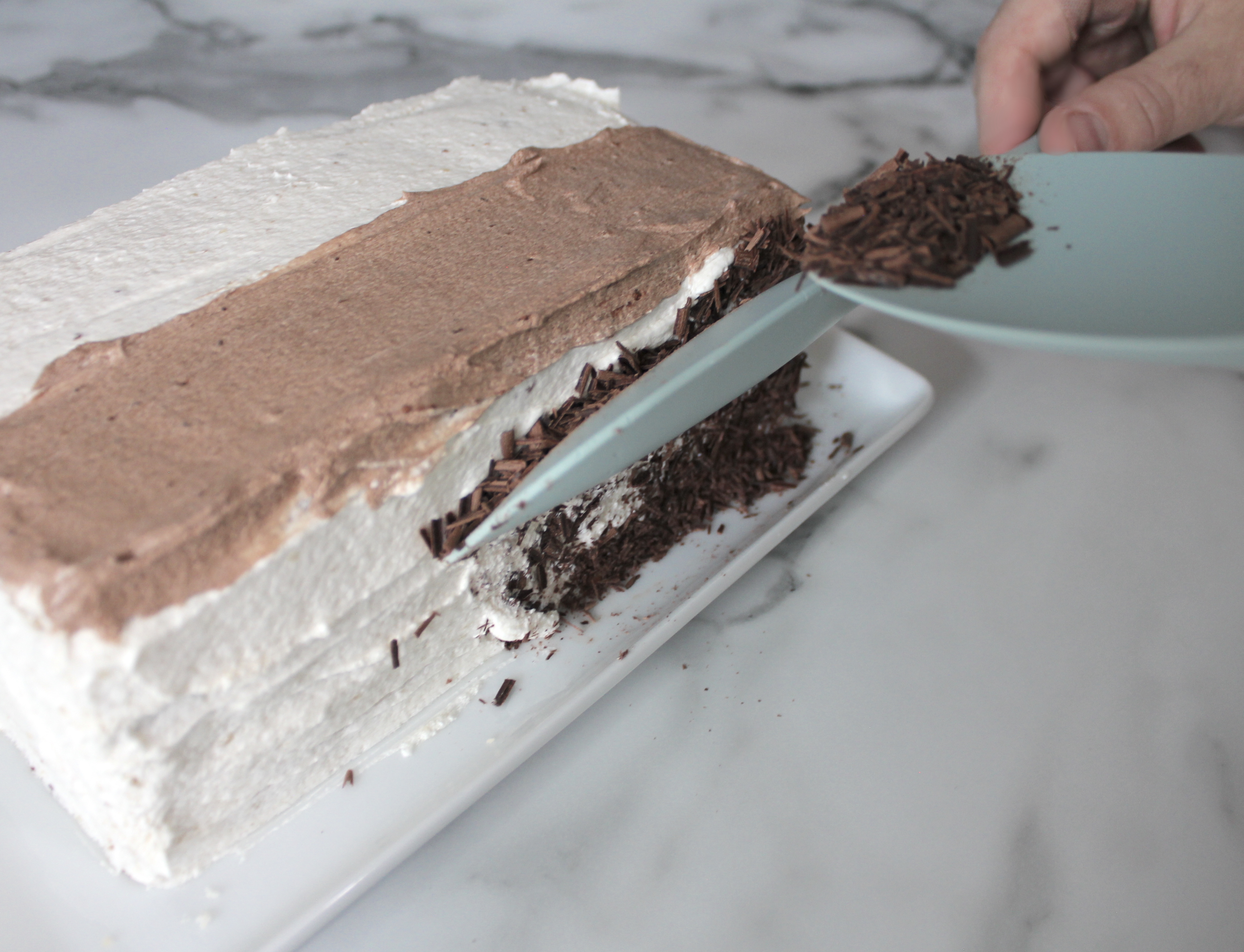 Using two spatulas to apply chocolate shavings.